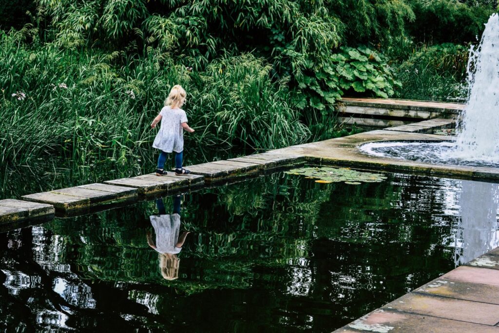 Un jardin. Une fillette marchant sur un ponton dans un parc, avec un jardin et un étang pour Berryfield